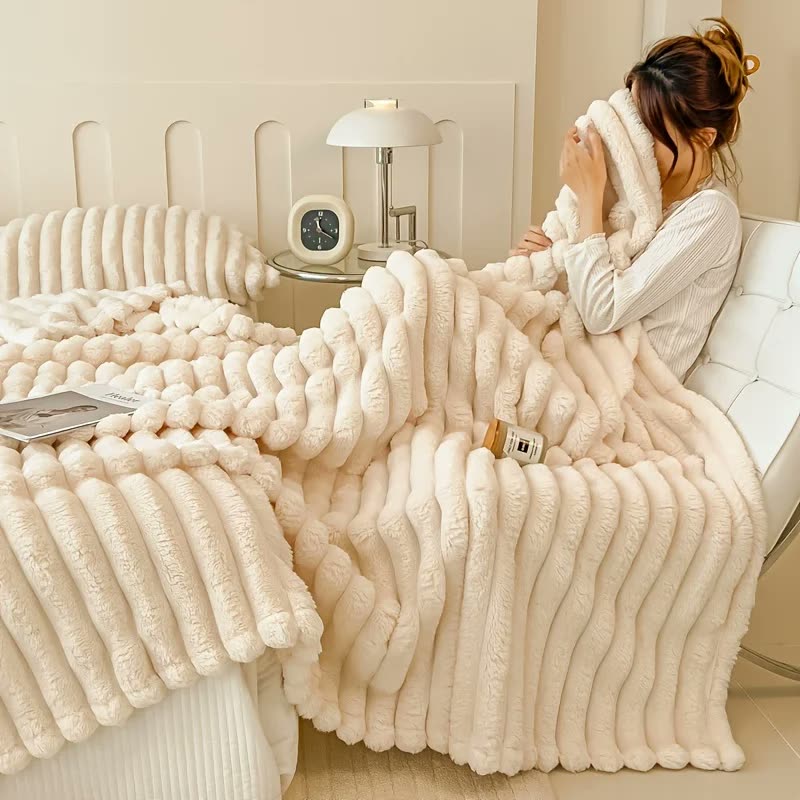 Une femme enveloppée dans un plaid blanc en fausse fourrure sur son lit